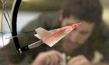 a model plane with colored coming off it is seen in foreground, person bending over concentrating in back